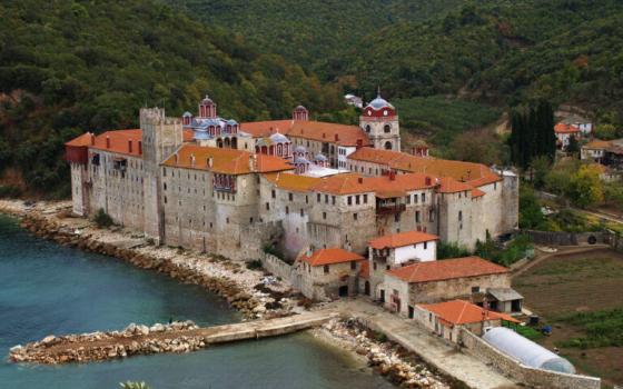 Large, ancient complex sits next to blue, sparkling lake or bay. 