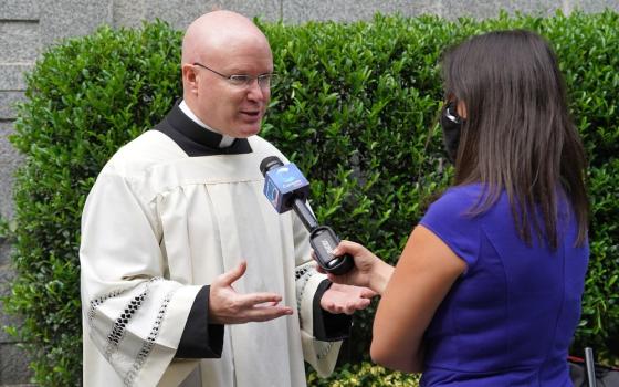 Landry, in choir dress, speaks outdoors to reporter.  