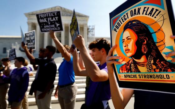 People stand holding signs in support of Apache Stronghold; Supreme Court building seen in background.