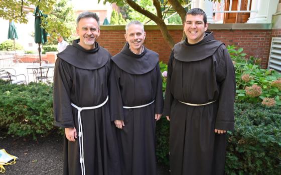 The three friars stand under a tree smiling. 