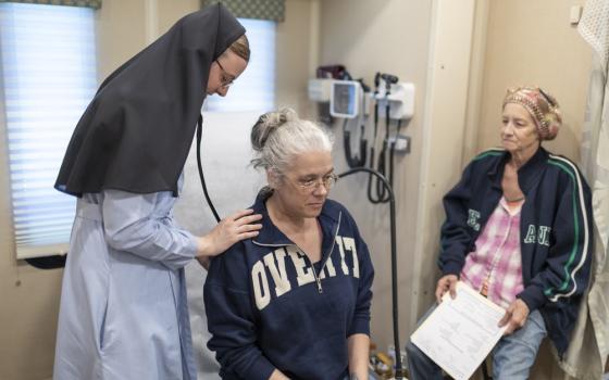 Sisters Mary Lisa, in habit, listens to patient's heart with stethoscope.