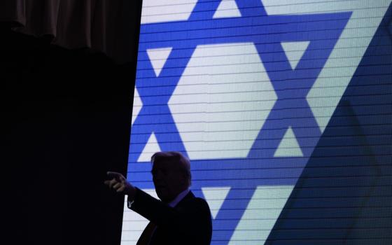 Trump silhouetted against illuminated stage background of the Star of David. 