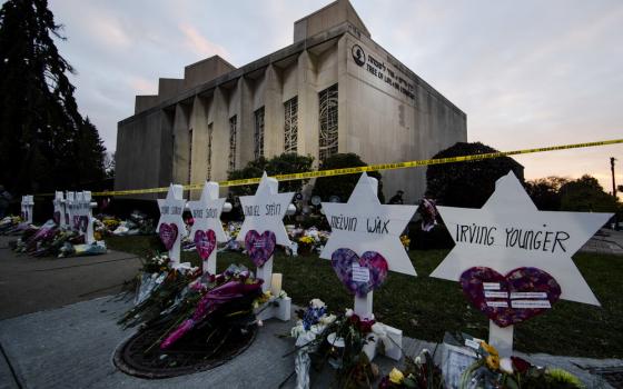 Small markers bear the names of the killed, in the background is the synagogue still marked with crime scene tape,