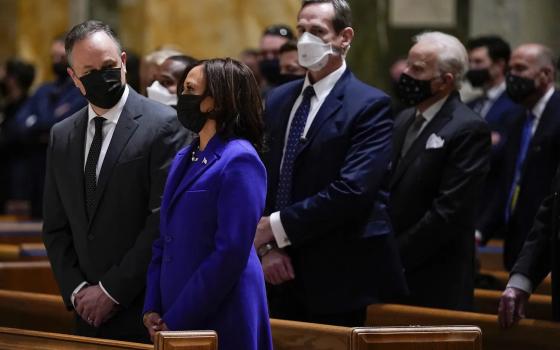 Harris, in blue suit and black face mask, stands in pew with hands crossed.