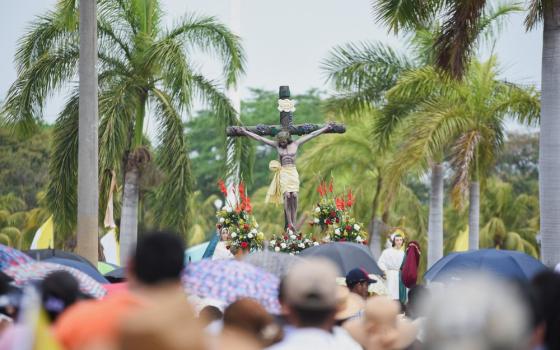 Crucifix on flowered float, framed by grove of palm trees.