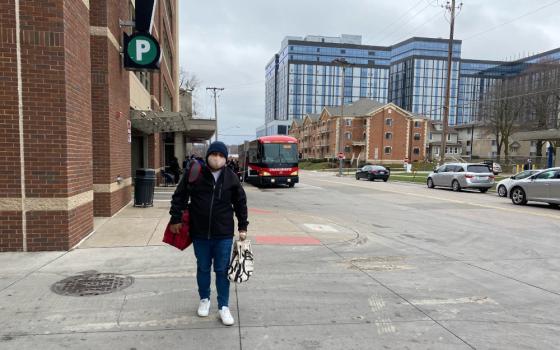 Man in a mask walking along a sidewalk toward camera