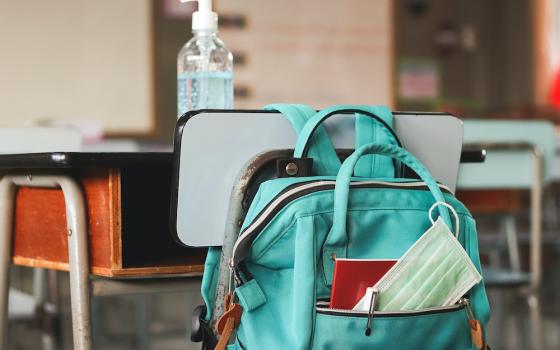 A disposable face mask is seen in a backpack hanging on a school desk holding a bottle of hand sanitizer. (Dreamstime/Phuttharak Chindarot)