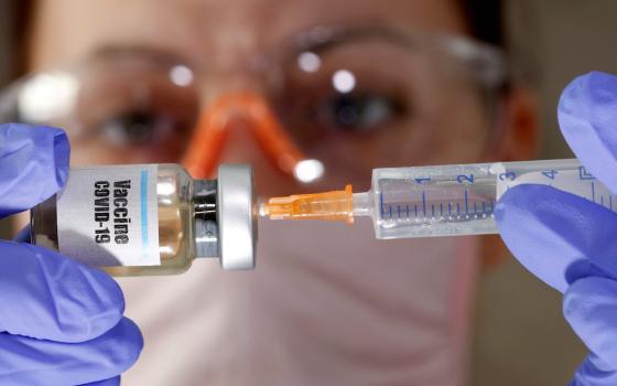 A woman holds a small bottle labeled with a "Vaccine COVID-19" sticker and a medical syringe in this photo illustration. (CNS Illustration/Reuters photo/Dado Ruvic)