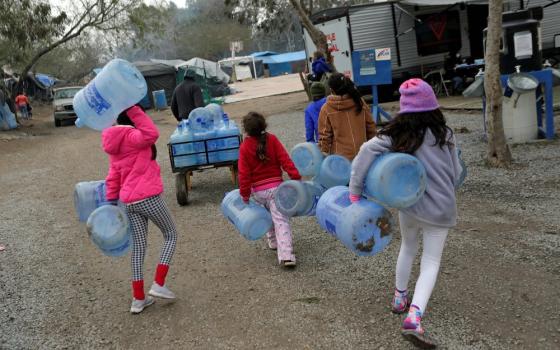 Children carry empty water containers inside a migrant encampment in Matamoros, Mexico, Feb. 18, 2021. (CNS/Reuters/Daniel Becerril)