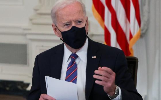 Joe Biden seated in black mask holding papers