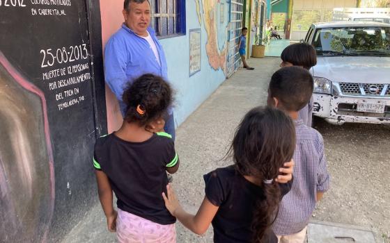 Children talking to a priest on a street by a colorfully painted wall