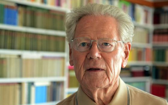 White haired man in glasses in front of books on a shelf