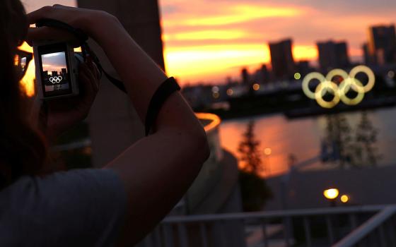 A person photographs the Olympic Rings in front of the skyline during sunset July 20 in Tokyo, three days ahead of the official opening of the 2020 Olympic Games. (CNS/Reuters/Kai Pfaffenbach)