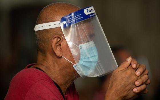 A man wearing a protective mask and face shield prays inside the Minor Basilica of the Black Nazarene in Manila, Philippines, Oct. 2, 2020, during the COVID-19 pandemic. (CNS/Reuters/Eloisa Lopez)