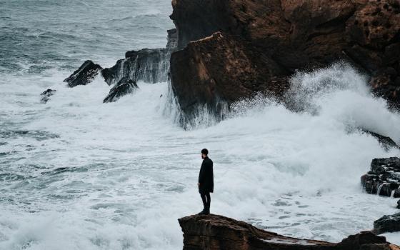 Man standing on rocky shore of Algeria (Unsplash/Benoumechiara)