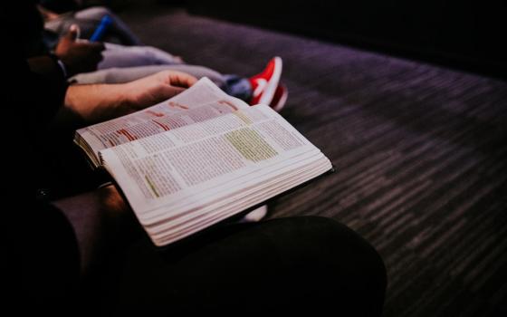 Bible page opened to Matthew, with highlights, in the hand of a person sitting on a park bench