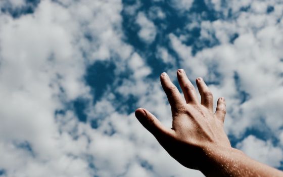 Hand reaching toward clouds in the sky (Unsplash/Jeremy Perkins)