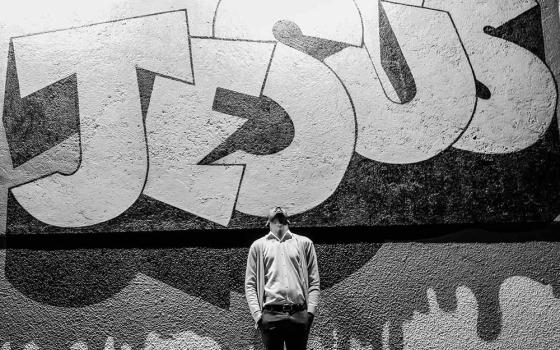 Man standing looking up in front of graffiti style lettering "Jesus"