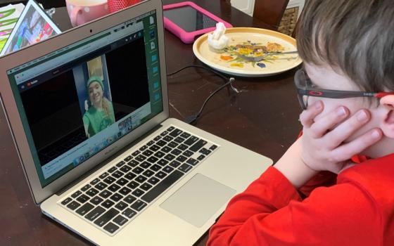 Jaxon, a second-grader at Holy Family Catholic Academy in Inverness, Illinois, watches a video from one of his teachers on a laptop at his dining room table. (Jamie Breeden)