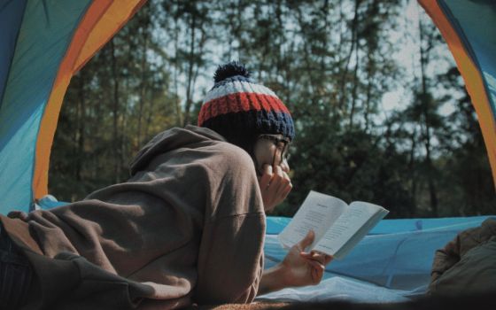 A person reading a book in a tent in the forest. (Unsplash/Lê Tân)