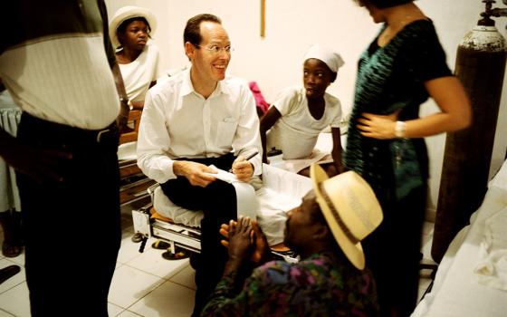 Dr. Paul Farmer sits with a young leukemia patient, Marta Cassmand, in Cange, Haiti, in January 2004. Marta's father, Sanoit Valceus (foreground), had cut a tendon in his hand and was asking Farmer for advice. (Newscom/PSG/St. Petersburg Times)