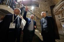 Three white men wearing clerical collars look up at the ceiling of an underground stone-lined space