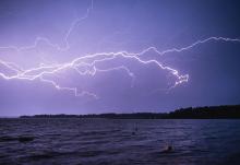 In this photo illustration lightning strikes across a night sky, lighting up a body of water below. (Unsplash/Niilo Isotalo)