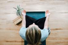 woman sits on cushion, with hands pointing upward