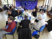 Men and women sit at round tables listening to presentation. 