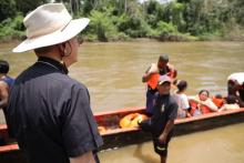 Bishop Seitz pictured from behind, watching migrants disembark from river canoes. 