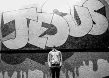 Man standing looking up in front of graffiti style lettering "Jesus"