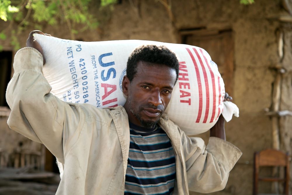 Man carries bag of wheat that says "USAID."