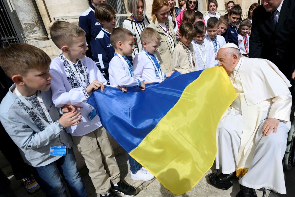 Pope Francis kisses a Ukrainian flag carried by a group of Ukrainian children.