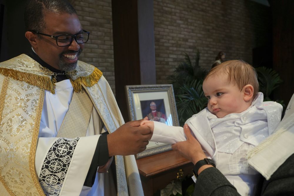 Ricky Malebranche, who was ordained as a priest June 7, holds the hand of 9-month-old Andres Roman Marquez after baptizing him at St. Louis Catholic Church in Alexandria, Va., May 24. (AP/Luis Andres Henao)