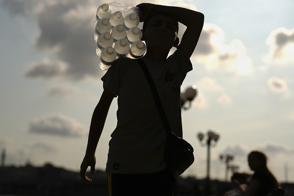 A young street vendor carries plastic bottles of water on his shoulder on a summer day, in Istanbul Aug. 8, 2025. (AP/Francisco Seco)