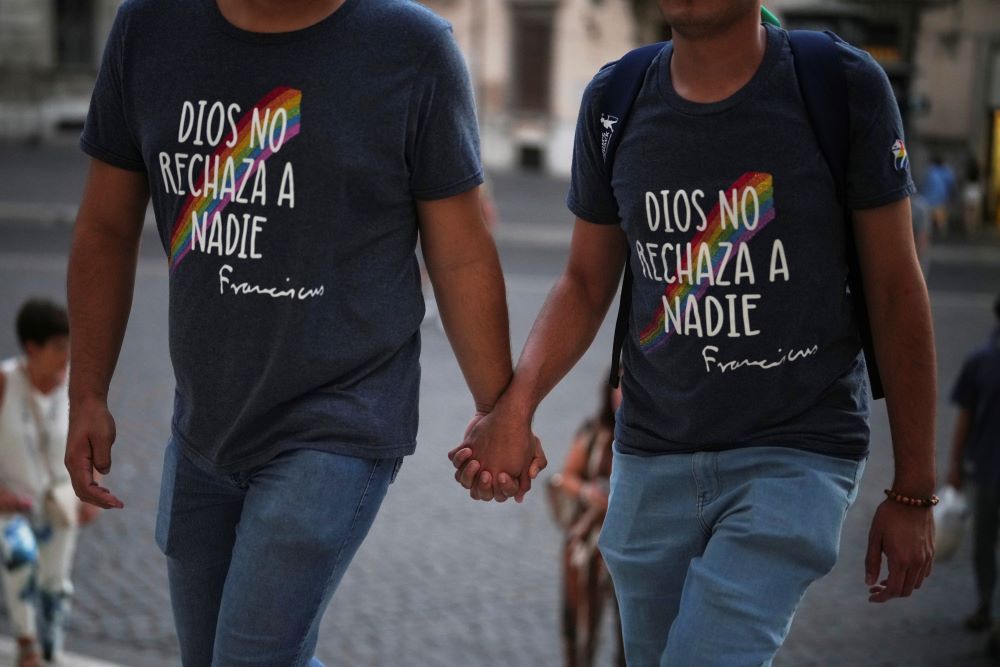 2 people hold hands and wear T-shirts reading "God does not reject anyone" in Spanish. 