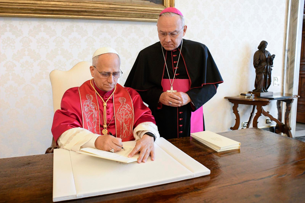 Pope Leo XIV signs his first apostolic exhortation, "Dilexi Te" ("I Have Loved You"), in the library of the Apostolic Palace at the Vatican Oct. 4, the feast of St. Francis of Assisi, as Archbishop Edgar Peña Parra, the substitute secretary for general affairs at the Vatican Secretariat of State, looks on. The exhortation was released Oct. 9. (OSV News/Reuters/Vatican Media)
