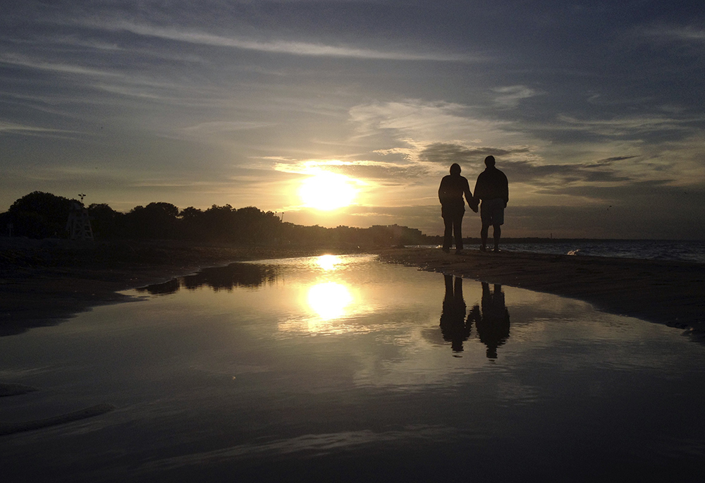 A couple is pictured in a file photo walking along Gillson Beach holding hands as the sun sets in Wilmette, Illinois. "Sometimes I come close to tears, not out of weakness, but from the exhaustion of seeing truth and kindness diminish in public life," writes NCR editor/publisher emeritus Thomas Fox. (OSV News/Reuters/Jim Young)
