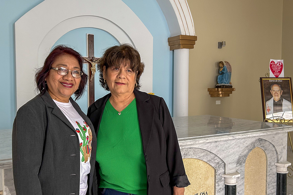 Lola Chávez, left, and Elena Lozada Seminario stand for a photo in front of the tomb of Augustinian Bishop John McKniff of Chulucanas, Peru, at St. Joseph the Worker Parish. (NCR photo/Justin McLellan)