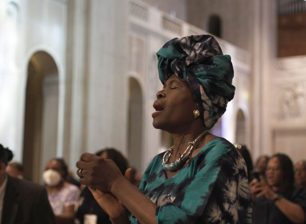 A Black woman sings or prays in still image from new film.