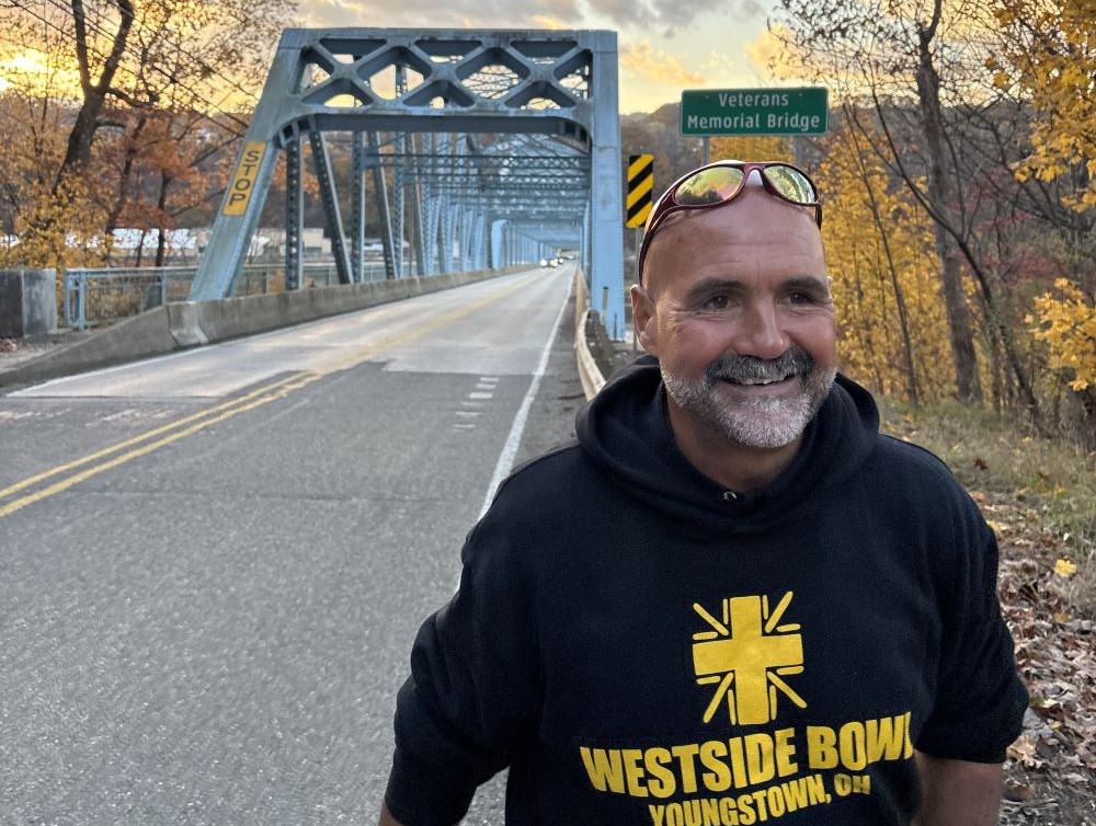 Fr. Gary Graf walks with bridge behind him. 