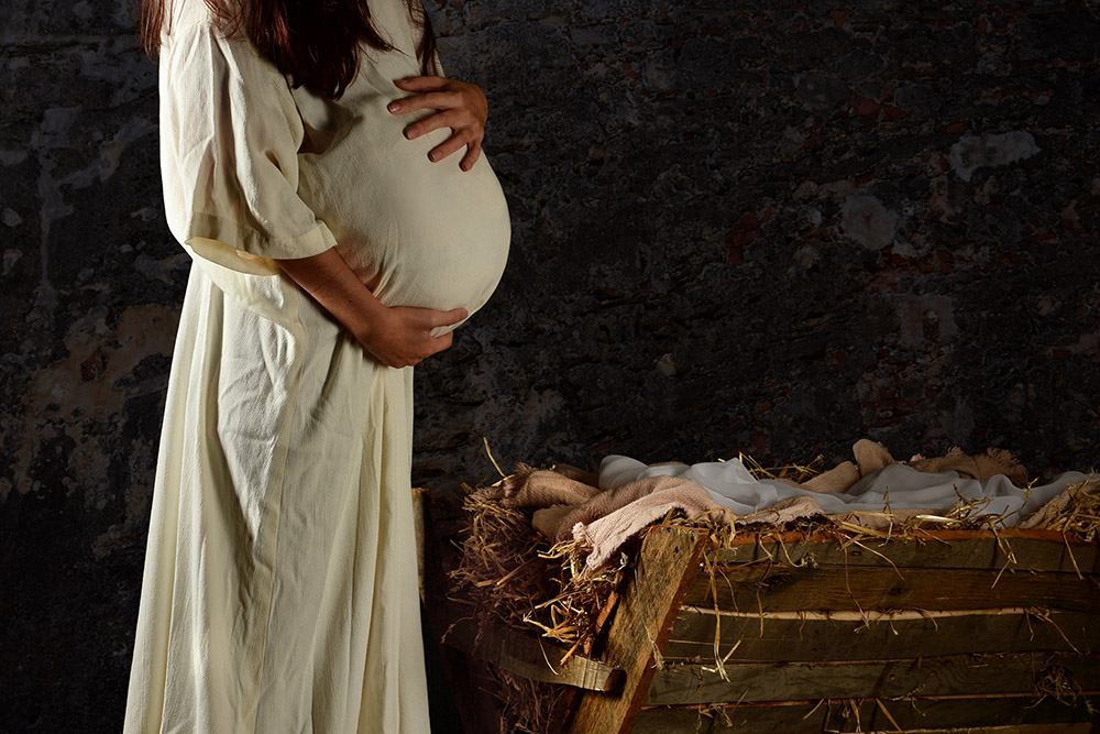 Pregnant Mary in a white robe stands next to the manger (Dreamstime/R. Gino Santa Maria)