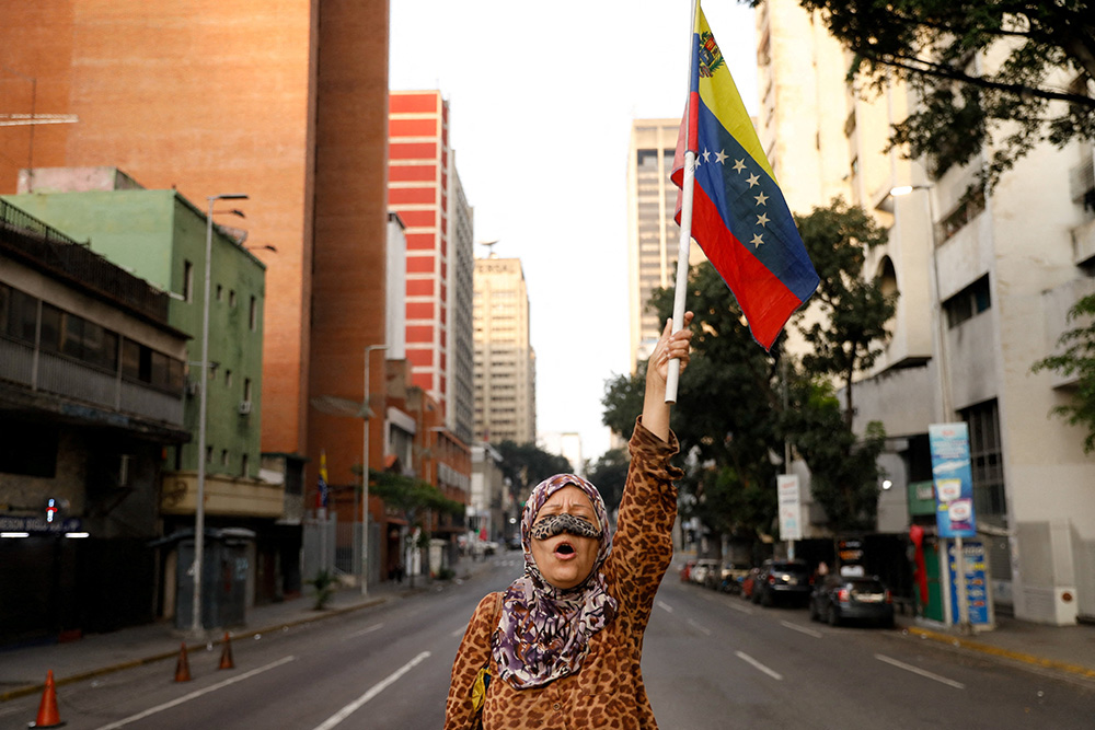 A supporter of Venezuelan President Nicolás Maduro holds a flag of Venezuela on a street near Miraflores Palace in Caracas, Jan. 3, 2026, after U.S. President Donald Trump said the U.S. has struck Venezuela and captured Maduro. (OSV News/Reuters/Leonardo Fernandez Viloria)