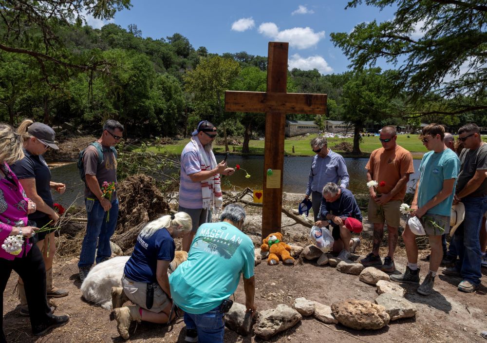 People pray after placing a cross by the Guadalupe River, across from Camp Mystic, following deadly flooding, in Hunt, Texas, July 10, 2025. (OSV News/Reuters/Umit Bektas)