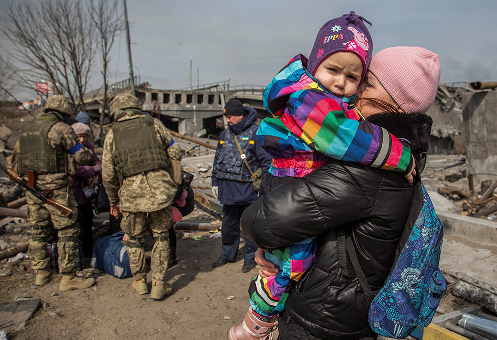 A woman holds a child next to a destroyed bridge during evacuation from Irpin, Ukraine, March 28, 2022, as Russia continued its attack on the country. (OSV News/Reuters/Oleksandr Ratushniak)