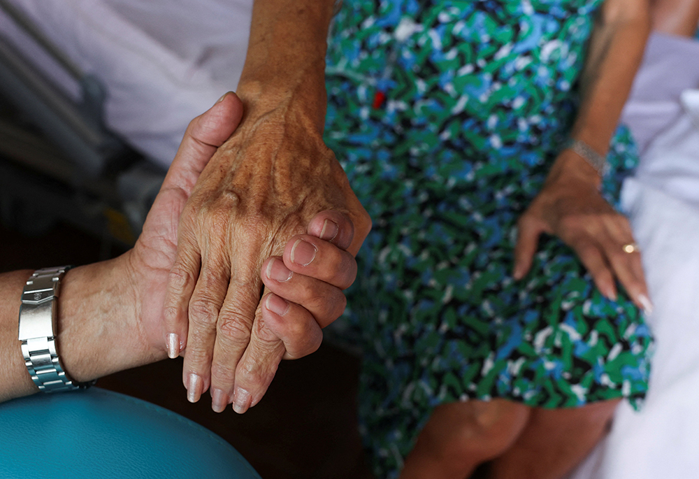 A nurse touches the hand of a patient at the palliative care unit of the Clinic St.-Elisabeth in Marseille, France, May 31, 2024. (OSV News/Reuters/Manon Cruz)
