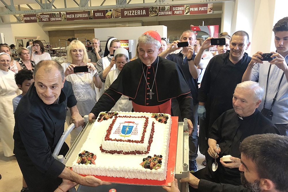 Cardinal Konrad Krajewski, the papal almoner, helps carry a cake as he hosts a dinner for the poor in the dining hall at the Vatican June 29, 2018. (CNS/Gianna Iasilli)