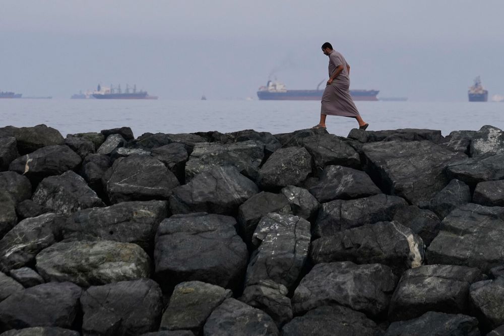 A man walks along the shore as oil tankers and cargo ships line up in the Strait of Hormuz, as seen from Khor Fakkan, United Arab Emirates, March 11, 2026. (RNS/AP/Altaf Qadri)