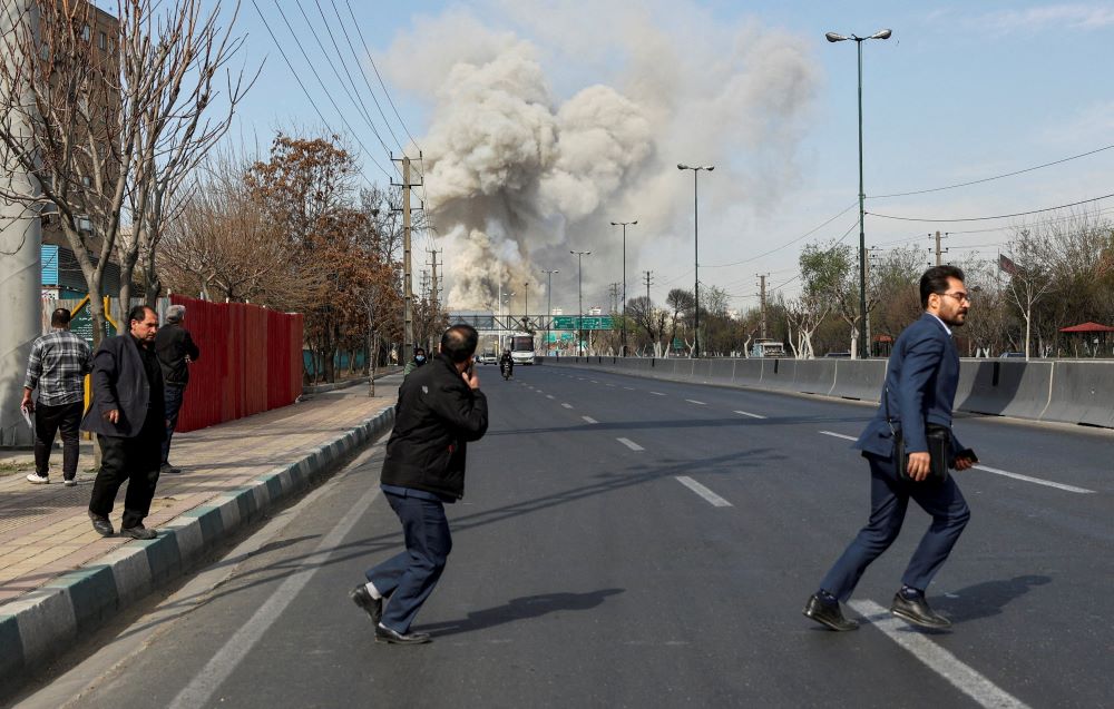 People run as smoke rises following an explosion in Tehran, Iran, March 5, 2026, following a strike on a police station, amid the U.S. and Israel-Iran war. (OSV News/WANA via Reuters/Majid Asgaripour)