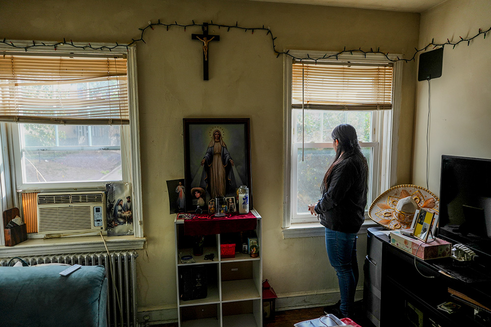 A parishioner of the Shrine of the Sacred Heart whose husband was detained by immigration agents looks out her home's window in Washington, D.C., Oct. 10, 2025. (AP/Luis Andres Henao)
